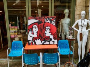 sur le devant d'une boutique de brocanteur, au cour du quartier, Grand Bayonne, une Toile est exposée sur table, entourée de chaise en plastique bleu